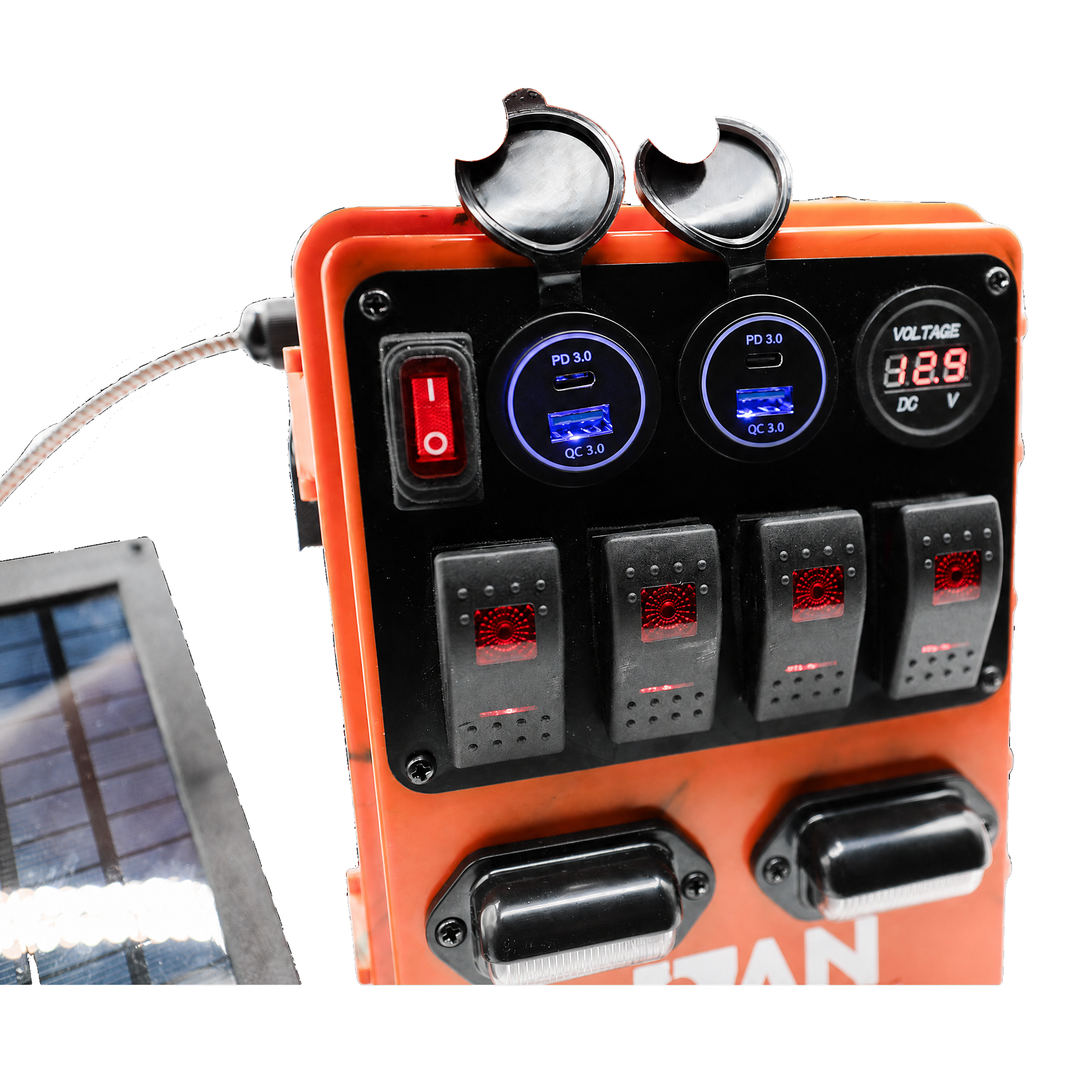 An orange solar power distribution panel with a black faceplate, featuring multiple rocker switches, two circular digital displays with blue backlighting, a red power switch, and two black terminal covers. A small solar panel is partially visible on the left against a white background.