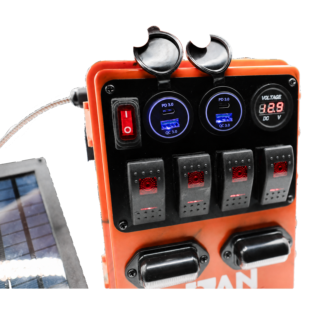 An orange solar power distribution panel with a black faceplate, featuring multiple rocker switches, two circular digital displays with blue backlighting, a red power switch, and two black terminal covers. A small solar panel is partially visible on the left against a white background.